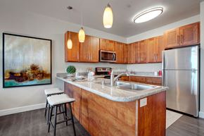 Salt Lake City apartment for rent - A kitchen here at Ritz Classic with warm wood cabinets, stainless steel appliances, gray countertops, pendant lights, and a compact island with two cushioned bar stools, providing a warm, cozy, open-concept feel.