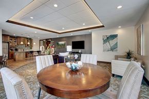 Salt Lake City apartment for rent - A spacious resident lounge here at Velo on the Boulevard with a round wood dining table, upholstered chairs, comfortable seating, wall-mounted TV, and an open community kitchen area, creating a warm, social space for gathering and relaxing.