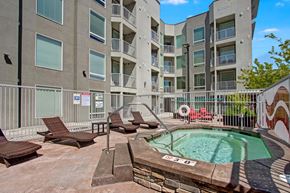 Salt Lake City apartment for rent - A private outdoor spa here at Velo on the Boulevard with a heated hot tub, metal handrails, surrounding lounge chairs, and a secured courtyard setting beside modern apartment buildings, creating a relaxing amenity space.