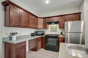 Salt Lake City apartment for rent - A modern kitchen here at Velo on the Boulevard with dark wood cabinets, light countertops, stainless steel refrigerator, black range and hood, and generous counter space, creating a clean, functional layout with a warm, contemporary feel.