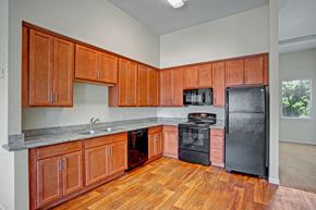 Wenatchee apartment for rent - A spacious kitchen here at 600 Riverside with warm wood cabinets, long countertops, black appliances, double sink, and wood-style flooring, creating a clean, functional cooking space with generous storage and prep area.