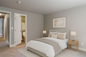 Lynnwood apartment for rent - A bedroom here at A'Cappella with soft neutral walls, a light upholstered bed with beige and white bedding, matching wood nightstands and lamps, and an open doorway to the ensuite bath for a bright, welcoming feel.