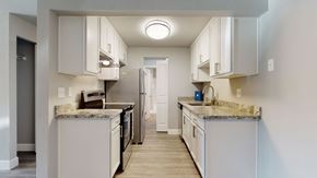 Lynnwood apartment for rent - A kitchen here at A'Cappella with bright white cabinets, speckled granite-style counters, stainless appliances, warm wood-look flooring, and a clean, modern layout with good overhead lighting.