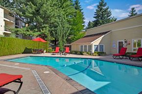 Bellevue apartment for rent - A refreshing outdoor pool here at Adagio featuring clear blue water, a spacious pool deck, and multiple red lounge chairs arranged for relaxing, with patio tables and umbrellas nearby, while surrounding greenery, mature trees, and adjacent community buildings create a private, resort-style setting for residents to enjoy warm days outdoors.