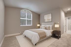 Kirkland apartment for rent - A serene bedroom here at Aspen Creek featuring a softly carpeted floor, a neatly made bed with neutral bedding and layered pillows, matching bedside tables with lamps, and minimalist wall art above the headboard, while a large arched window with blinds brings in natural light and a hallway entry adds a sense of space and flow.