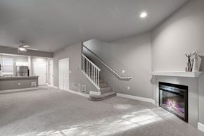 Kirkland apartment for rent - A spacious open living room here at Aspen Creek featuring plush wall-to-wall carpet, a staircase with white railing leading to the upper level, and a tiled fireplace with a clean mantel, while recessed lighting and a ceiling fan complement the open layout that flows toward the kitchen and entryway.
