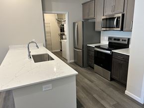 Leavenworth apartment for rent - A modern kitchen here at Autumn Haus featuring a spacious white quartz-style island with an undermount sink, wide plank flooring, gray cabinetry, and sleek appliances, complemented by a pantry or utility room visible through an open doorway that adds extra storage and everyday convenience.