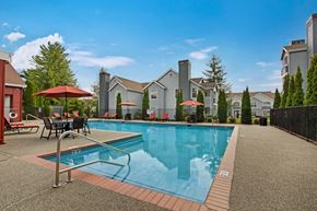 Everett apartment for rent - A swimming pool surrounded by a patio with chairs and umbrellas.