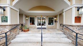 Shoreline apartment for rent - A welcoming leasing office entrance here at Forest Hills featuring an arched covered entryway, stone-accented columns, and light siding. Concrete steps with handrails lead to glass double doors, flanked by windows, exterior wall lights, and signage, creating a polished and approachable arrival for residents and guests.