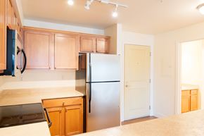 Shoreline apartment for rent - A compact kitchen here at Forest Hills featuring light wood cabinets, neutral countertops, and a full appliance setup including a refrigerator, range, and microwave. Overhead track lighting brightens the space, and a nearby doorway leads toward the entry and adjacent rooms, creating a clean and functional layout.