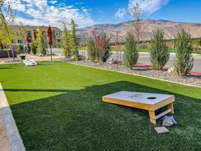 Wenatchee apartment for rent - A landscaped outdoor lawn here at LIVEasy Street featuring a cornhole game set on vibrant green turf, surrounded by manicured shrubs, young trees, and stone accents. The open space offers mountain views, nearby patio seating with umbrellas, and a relaxed setting designed for outdoor games and social gatherings.