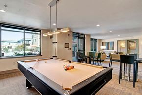 Seattle apartment for rent - A modern resident lounge here at Leilani on Greenwood featuring a billiards table centered beneath contemporary pendant lighting, with large windows providing natural light, adjacent seating and dining areas, and a comfortable open layout designed for socializing and relaxation.