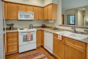 Everett apartment for rent - A welcoming kitchen here at Portsmith showcasing light wood cabinetry, neutral countertops, a double-basin sink, a dishwasher, and a built-in microwave above the range, complemented by warm wood-style flooring, simple countertop décor, and an open pass-through that connects the kitchen to the adjacent living space.