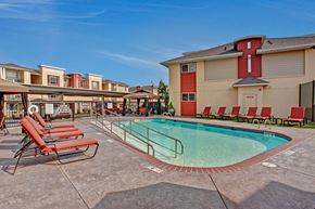 Wenatchee apartment for rent - A sunny outdoor pool here at Riverside 9 with clear water, red lounge chairs, shaded seating areas, and a welcoming community setting.