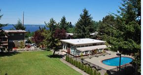 Federal Way apartment for rent - A scenic outdoor pool area here at Soundview with clear blue water, clubhouse, open green lawn, and beautiful water views surrounded by trees.