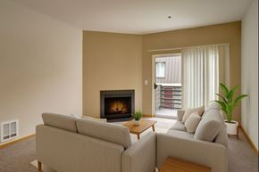 Seattle apartment for rent - A welcoming living room here at St. James Tower with beige sofas, a cozy fireplace, soft carpet, sliding glass door to a private balcony, and a green plant adding warmth and comfort.