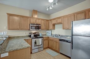 Moses Lake apartment for rent - A warm kitchen here at The Vintage with rich wood cabinets, speckled countertops, and stainless steel appliances including a refrigerator, stove, microwave, and dishwasher. A raised breakfast bar with pendant lighting creates a cozy and inviting dining space.