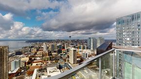 Seattle apartment for rent - A cityscape with a mix of modern and older buildings, a cloudy sky, and a body of water in the distance.