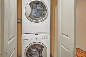 Kenmore apartment for rent - A laundry area here at Vermont featuring a stacked washer and dryer tucked behind double doors, offering a convenient, compact, and practical in-home laundry space.