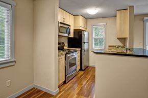 Kenmore apartment for rent - A kitchen here at Vermont featuring light wood cabinets, stainless steel appliances, breakfast bar, and warm wood flooring, creating a bright, efficient, and welcoming cooking space.
