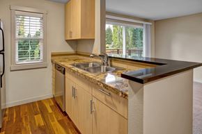 Kenmore apartment for rent - A kitchen here at Vermont featuring light wood cabinetry, granite countertops, double sink, breakfast bar, and warm wood flooring, creating a bright, modern, and welcoming space with a pleasant balcony view.