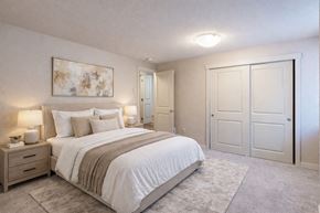 Kenmore apartment for rent - A bedroom here at Vermont featuring soft carpet, large closet doors, neutral bedding, bedside tables with lamps, and abstract wall art, creating a cozy, calm, and inviting retreat.
