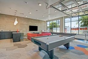 Seattle apartment for rent - A game lounge here at Vive featuring a sleek pool table, vibrant red sofa, dark entertainment bar, modern pendant lights, and large bright windows creating a stylish, inviting atmosphere.