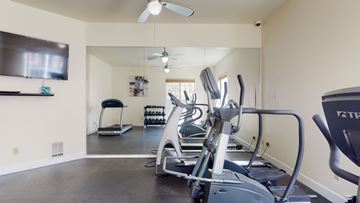 Issaquah apartment for rent - A spacious home gym with a treadmill, elliptical machines, and a television.