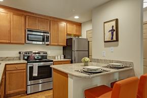 Issaquah apartment for rent - A cozy kitchen here at Windsong featuring warm wood cabinetry, stainless steel appliances, and bright orange barstools. Welcoming layout with a breakfast bar, clean finishes, and inviting, functional design.