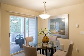 Issaquah apartment for rent - A bright dining area here at Windsong featuring a glass table, beige upholstered chairs, and an amber centerpiece vase. Welcoming layout with sliding door access to a private balcony and soft, natural light.