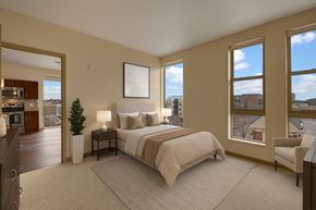 Milwaukee apartment for rent - A bright bedroom here at Avenir featuring soft neutral bedding, warm beige walls, and large sunny windows. Matching nightstands with lamps and a cozy accent chair create a calm, welcoming, and comfortable retreat.