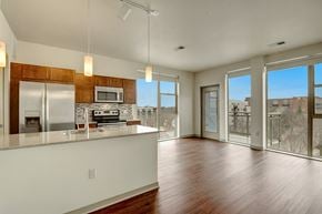 Milwaukee apartment for rent - A bright open living room and kitchen here at Avenir featuring warm wood cabinets, stainless steel appliances, and large windows. Rich wood floors and abundant natural light create a spacious, modern, and welcoming atmosphere.
