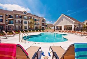 Madison apartment for rent - A large swimming pool surrounded by lounge chairs and umbrellas in front of a building.
