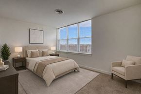 Milwaukee apartment for rent - A bright bedroom here at Latitude featuring neutral bedding, dark wood nightstands, and a soft area rug, complemented by a cozy accent chair and large sunlit windows creating a calm, welcoming atmosphere.