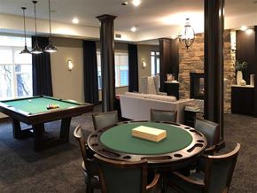 Shorewood apartment for rent - A game room here at Oaks of Shorewood featuring a green poker table, classic pool table, stone fireplace, and comfortable seating, creating a warm, inviting, and social entertainment space.