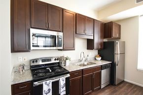 Shorewood apartment for rent - A kitchen here at Oaks of Shorewood featuring rich dark wood cabinets, stainless steel appliances, light granite countertops, and warm flooring, creating a bright, modern, and inviting cooking space.