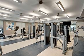 Milwaukee apartment for rent - A modern fitness center here at River House including weights and strength training equipment, encompassed in an open, bright, and motivating workout envrionment.