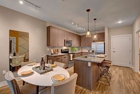 Milwaukee apartment for rent - A modern kitchen and dining area here at River House featuring warm wood cabinets, a kitchen island with bar stools, and a round white dining table, creating a bright, stylish, and welcoming space.