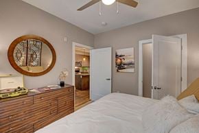 Milwaukee apartment for rent - A cozy bedroom here at River House featuring a white bed with warm gold pillows, a large wooden dresser sits across the bed with a rounded mirror, and a ceiling fan light brightening the space.
