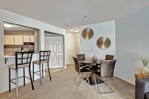 Germantown apartment for rent - A cozy dining area here at River’s Cove with a round table, brown upholstered chairs, and gold wall accents. The breakfast bar with black stools adds a welcoming space for casual dining and entertaining.
