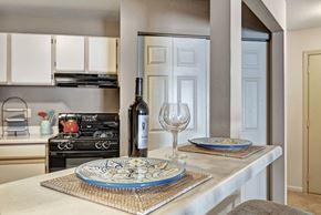 Germantown apartment for rent - A bright kitchen here at River’s Cove featuring a breakfast bar with decorative blue plates, wine glass, and bottle. Light cabinetry and an open pass-through create a clean, inviting space perfect for casual dining.