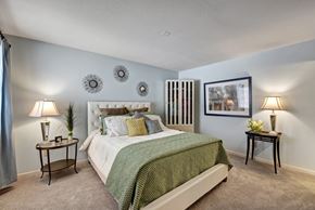 Germantown apartment for rent - A cozy bedroom here at River’s Cove featuring a plush bed with green bedding, soft carpet, and calming blue walls. Matching lamps and tasteful décor create a warm, inviting retreat perfect for relaxing.
