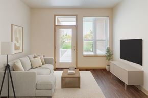 Madison apartment for rent - A bright living room here at Royster Commons with warm wood flooring, large windows, and a glass door leading outside. A cozy seating area and modern layout create a clean and inviting atmosphere.