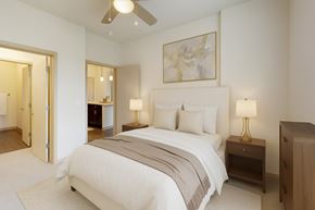 Madison apartment for rent - A bright bedroom here at Royster Commons with soft carpet, cream walls, and a ceiling fan for added comfort. A connected bathroom and warm lighting create a comfortable and inviting atmosphere.