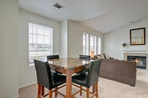 Milwaukee apartment for rent - A bright dining area here at St. James Place with soft beige carpet, large windows, and a modern dining table. A nearby fireplace and open living space create a warm and inviting atmosphere.