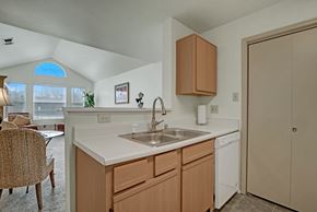 Milwaukee apartment for rent - A bright kitchen here at St. James Place with light wood cabinets, white countertops, and a double-basin sink. A breakfast bar opens to the living room, where large windows and high ceilings create an open and inviting atmosphere.