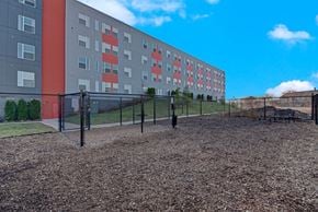 Milwaukee apartment for rent - A large building with a red and grey facade is behind a black fence.