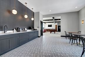 Fitchburg apartment for rent - A modern coffee bar here at The Lafayette with sleek dark cabinets, a beverage station, and pendant lighting. A patterned tile floor and nearby lounge and game area create a stylish, social atmosphere.