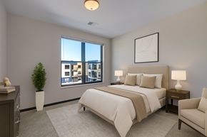 Fitchburg apartment for rent - A peaceful bedroom here at The Lafayette featuring soft neutral bedding, matching nightstands with lamps, a light area rug, a cozy accent chair, and a large window bringing in bright, refreshing natural light.