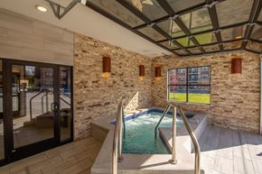 Deforest apartment for rent - A relaxing spa room here at The Park featuring a bubbling hot tub, stone accent walls, large windows, glass garage-style door, and warm lighting, creating a luxurious and tranquil retreat space.